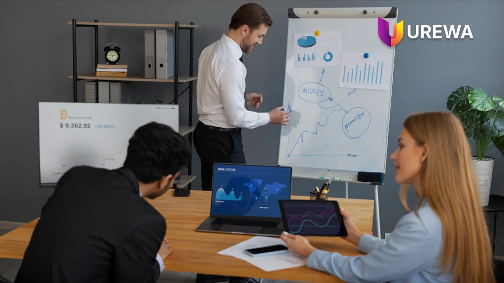 A sales team reviewing pipeline performance and business strategy together in a meeting room, working through charts on a whiteboard, laptop and tablet during a forecast review